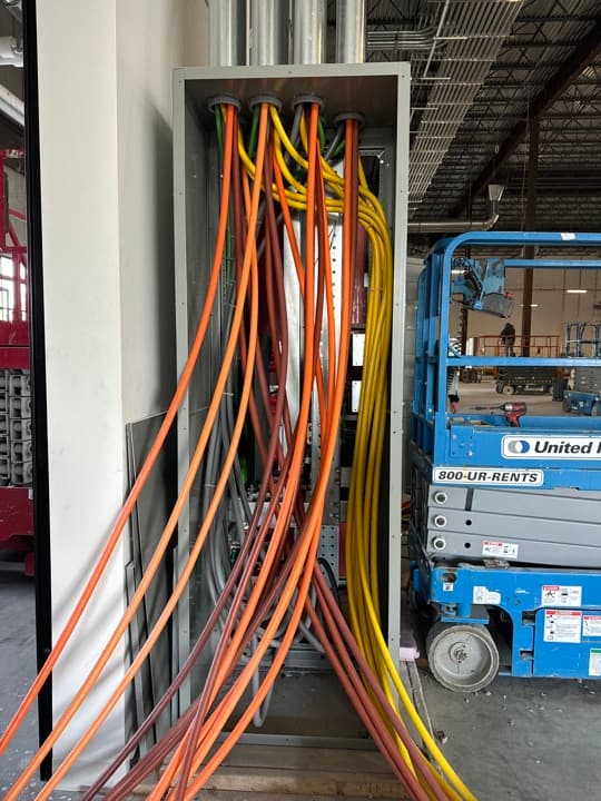 Commercial cable tray exiting a long pull box with bundled feeders running toward the equipment, boom lift staged in the background.