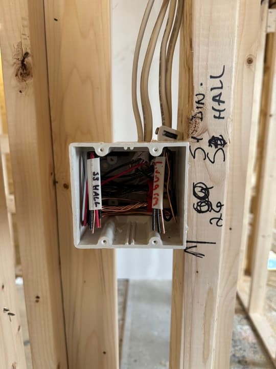 New-construction outlet rough-in with circuit destinations labeled in pen on the stud — Living Rm, S3 Hall — wires stripped and folded into the device box.