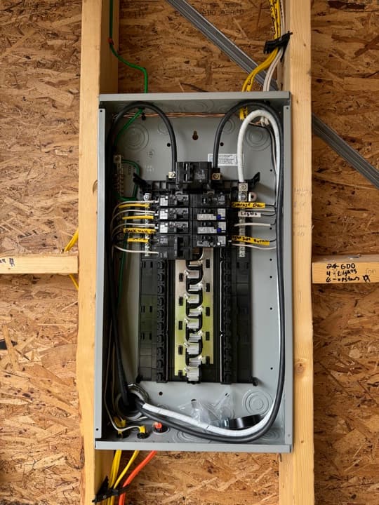 Residential sub-panel finished between studs with twenty-amp breakers and neat homeruns.