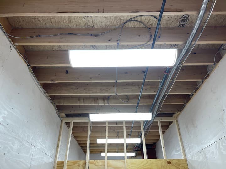 Temporary construction lighting hung along framed rafters with EMT and MC overhead during rough-in.