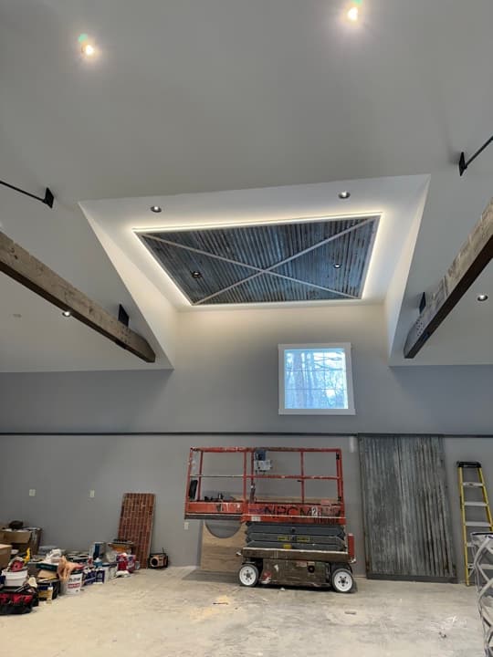 Residential cathedral entryway with a coffered ceiling feature, corrugated metal panel, recessed cove lighting around it, and recessed cans on the surrounding ceiling.