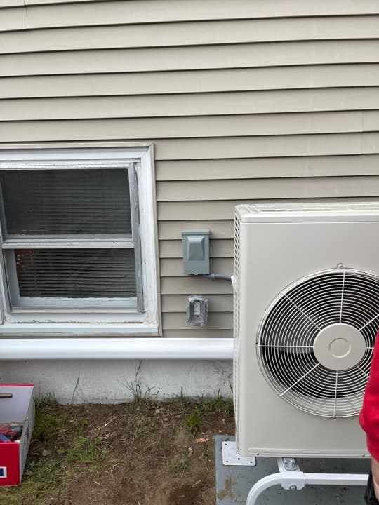 Mini-split outdoor condenser mounted on the side of a home with disconnect boxes installed neatly in line.