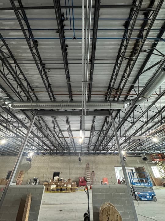 High-bay commercial warehouse interior with overhead conduits and industrial process piping above tall storage racking.